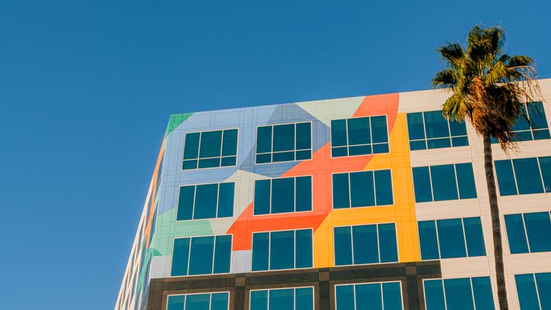 A brightly colored building photographed at upwards angle. there's a palm tree in front of it to the right of the image.