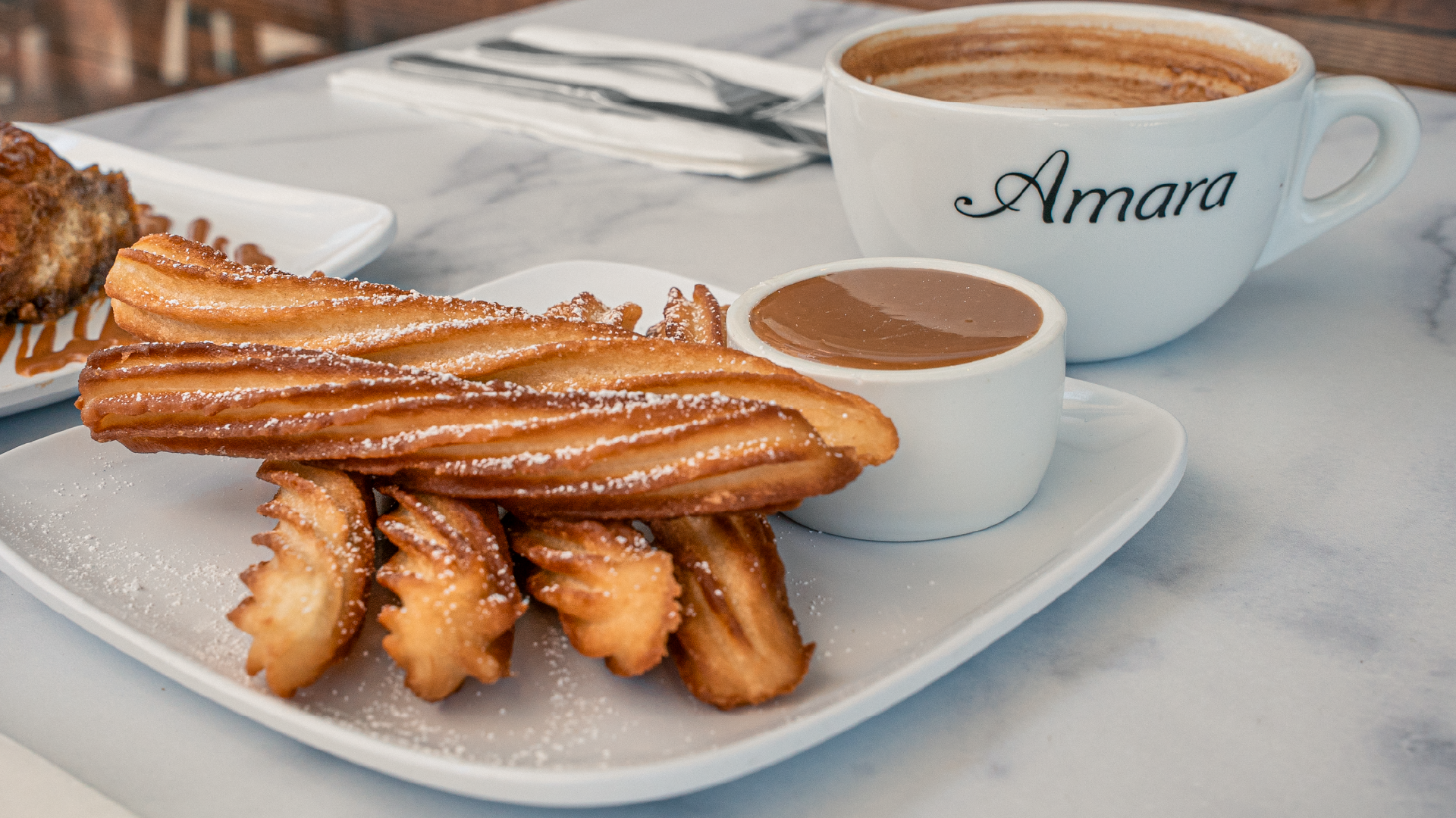 Amara Cafe – plate of churros with a cup of thick hot chocolate in an Amara-branded mug.