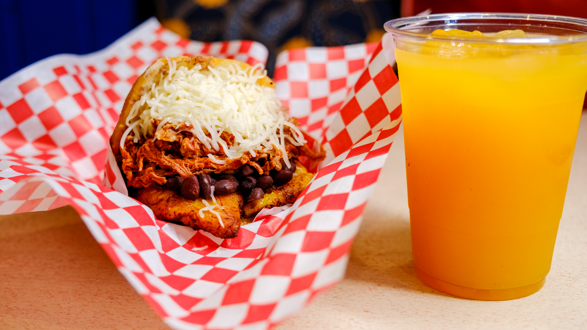 Venezuelan Chamo Cuisine – arepa filled with shredded beef, black beans and cheese in a red checkered basket, with a passion fruit drink.