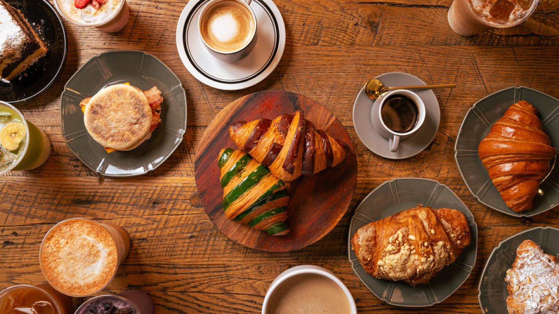 Home Brewed Bar – overhead spread of lattes, espresso drinks, croissants and pastries on a wooden table.