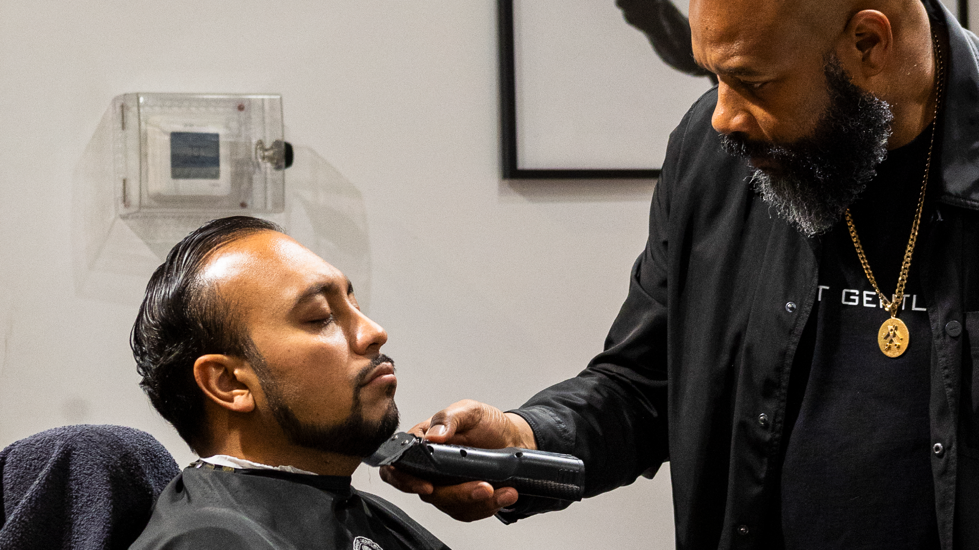 Perfect Gentleman Salon – barber trimming a client's beard with clippers in the barber chair.
