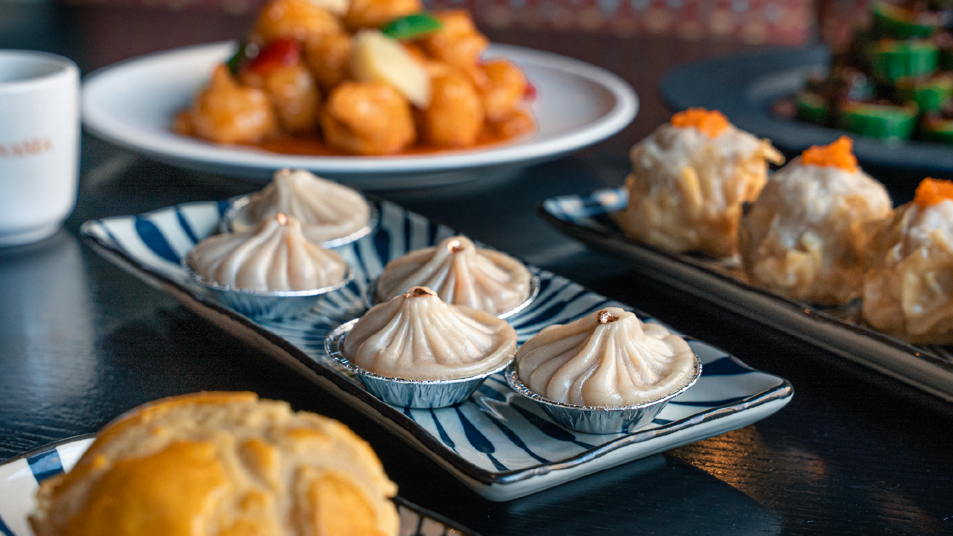 Lunasia – plates of dim sum including shumai, dumplings and buns on a dark table.