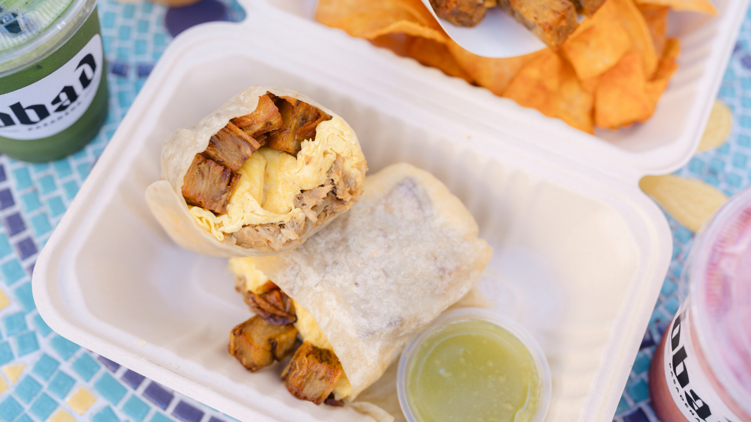 Breakfast Burritos All Day – breakfast burrito in a takeout box with roasted potatoes, tortilla chips and salsa verde.